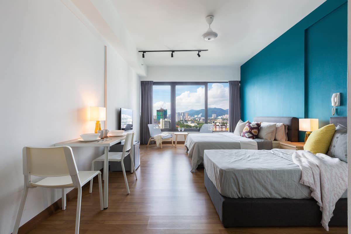 A modern hotel room with a large window, a desk, two beds, and a chair.