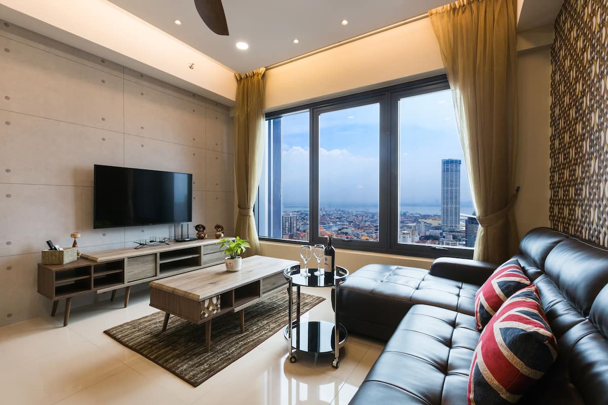 A modern living room with a large TV, a sofa, and a view of a cityscape through large windows.