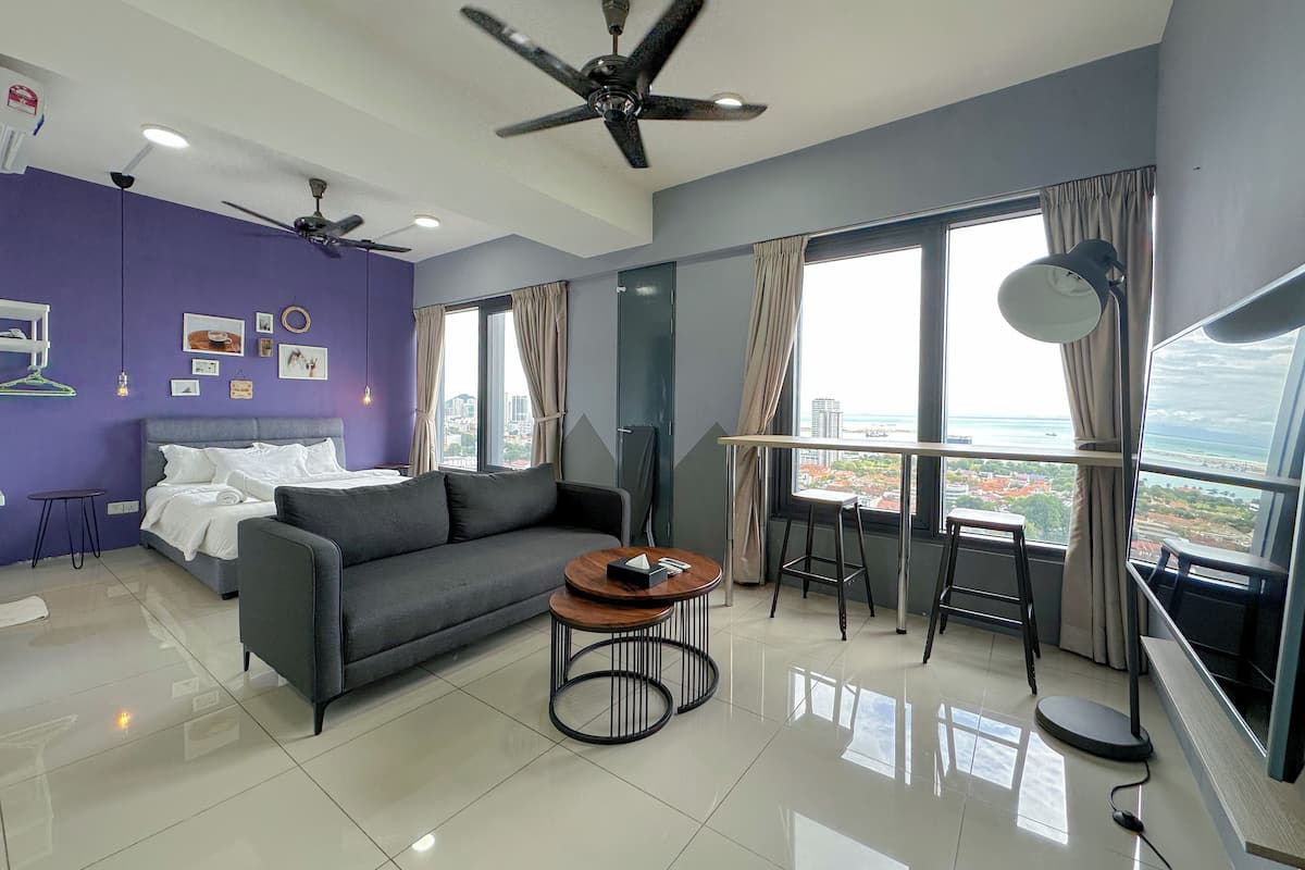 A modern living room with a sofa, a coffee table, and a balcony with a view of the city and ocean.