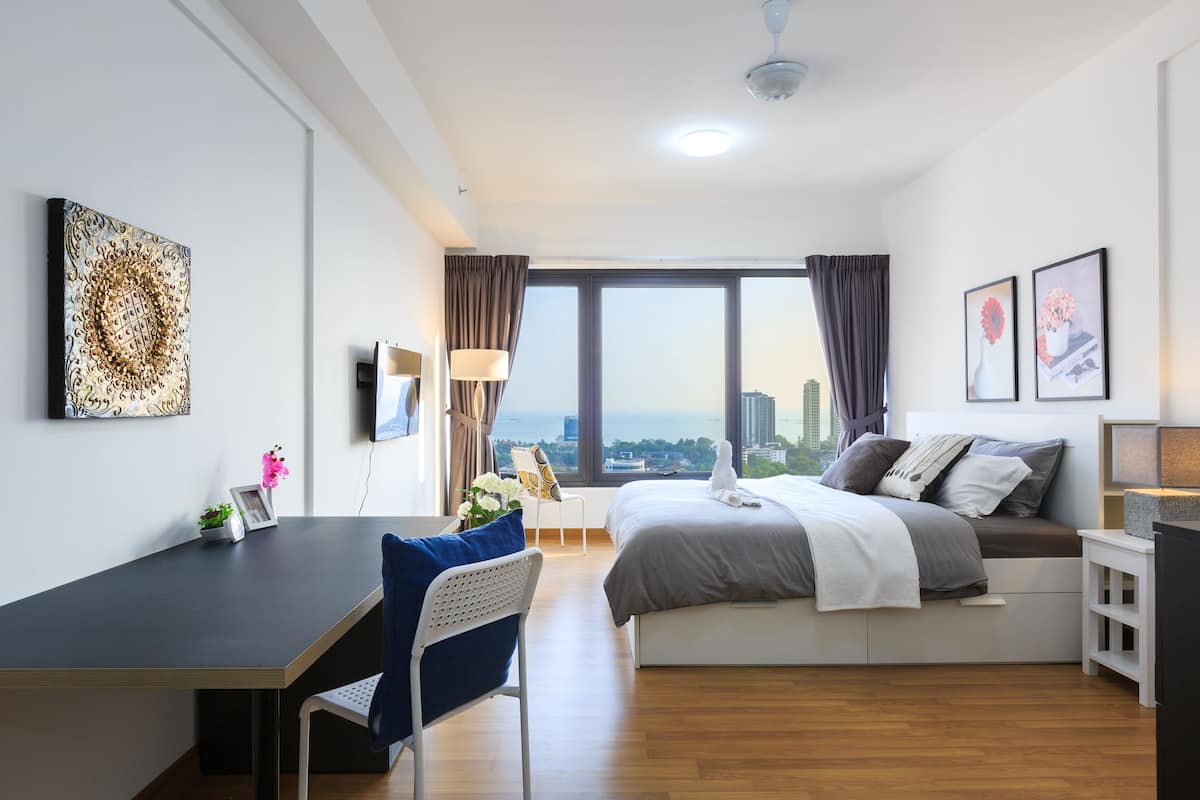 A modern hotel room with a bed, a desk, a chair, and a large window offering a city view.