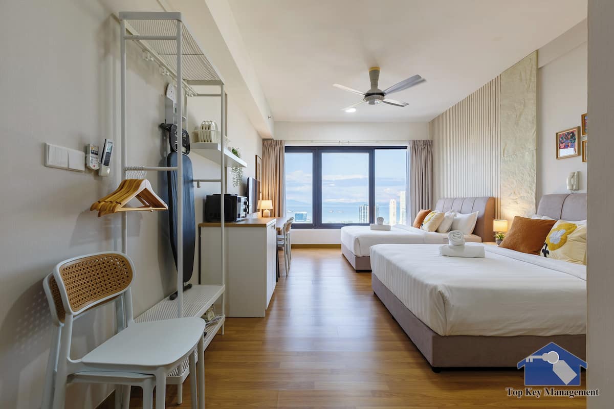A hotel room with a bed, a desk, a chair, a wardrobe, and a view of the sea.