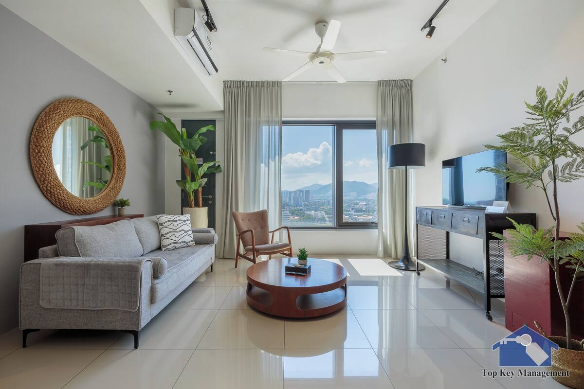 A modern living room with a sofa, armchair, round coffee table, and a large window with a city view.