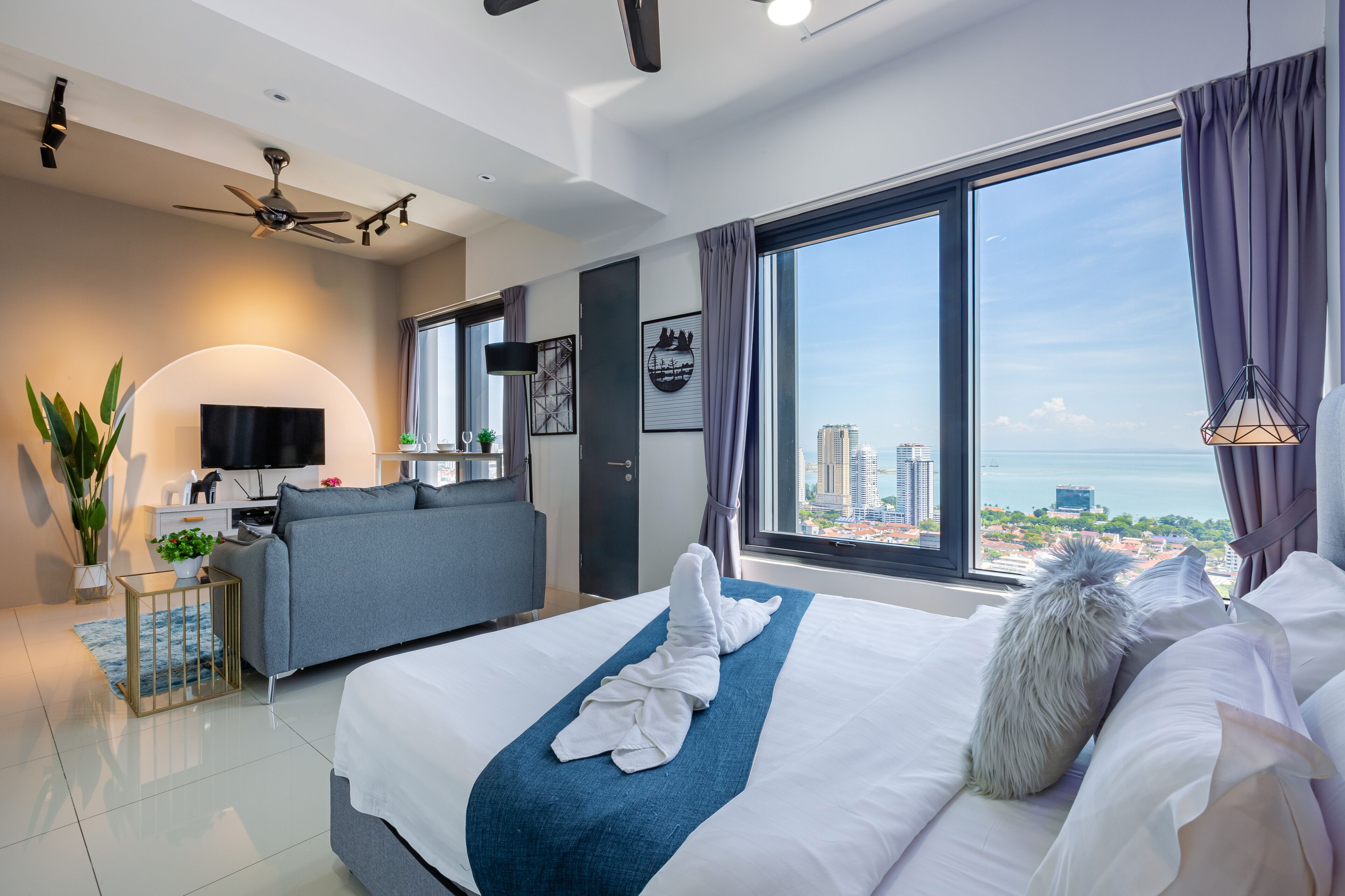 Habitación de hotel moderna con una cama grande, un sofá, un televisor y vistas a la ciudad.