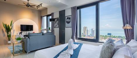 Habitación de hotel moderna con una cama grande, un sofá, un televisor y vistas a la ciudad.