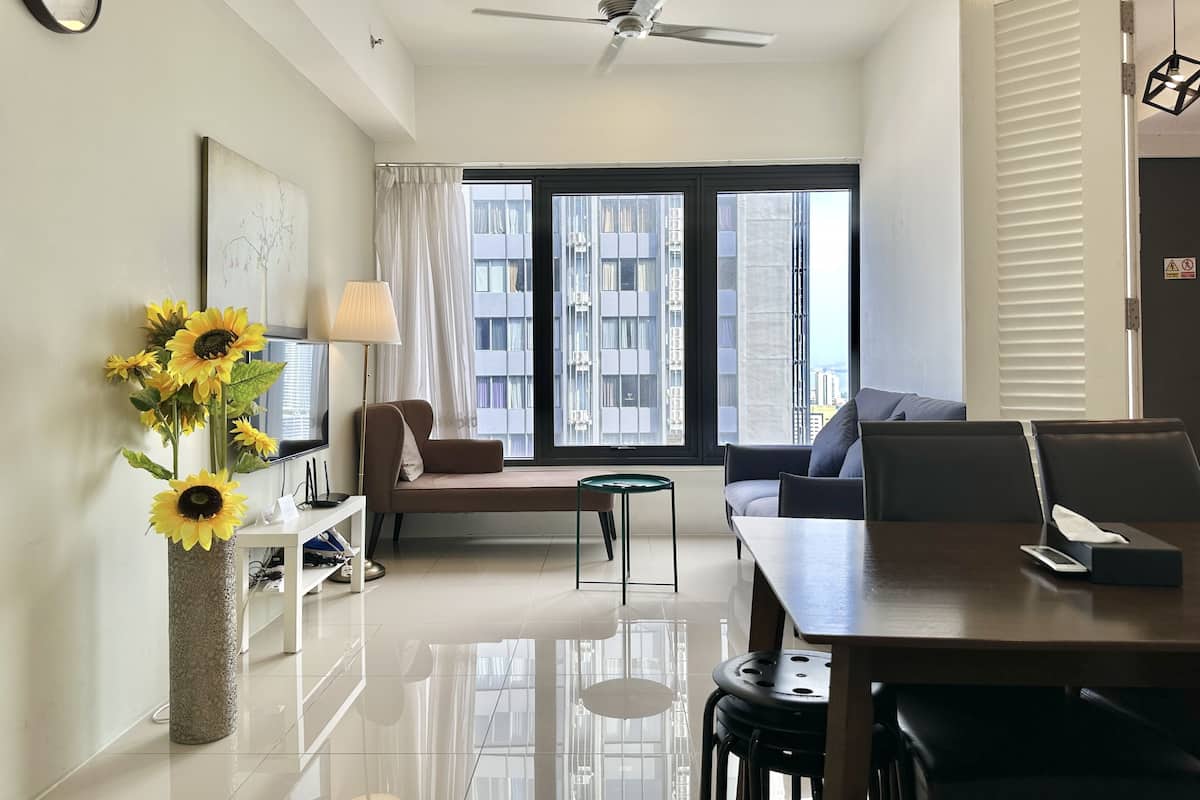 A modern living room with a sofa, a dining table, a TV, and a large window with blinds.