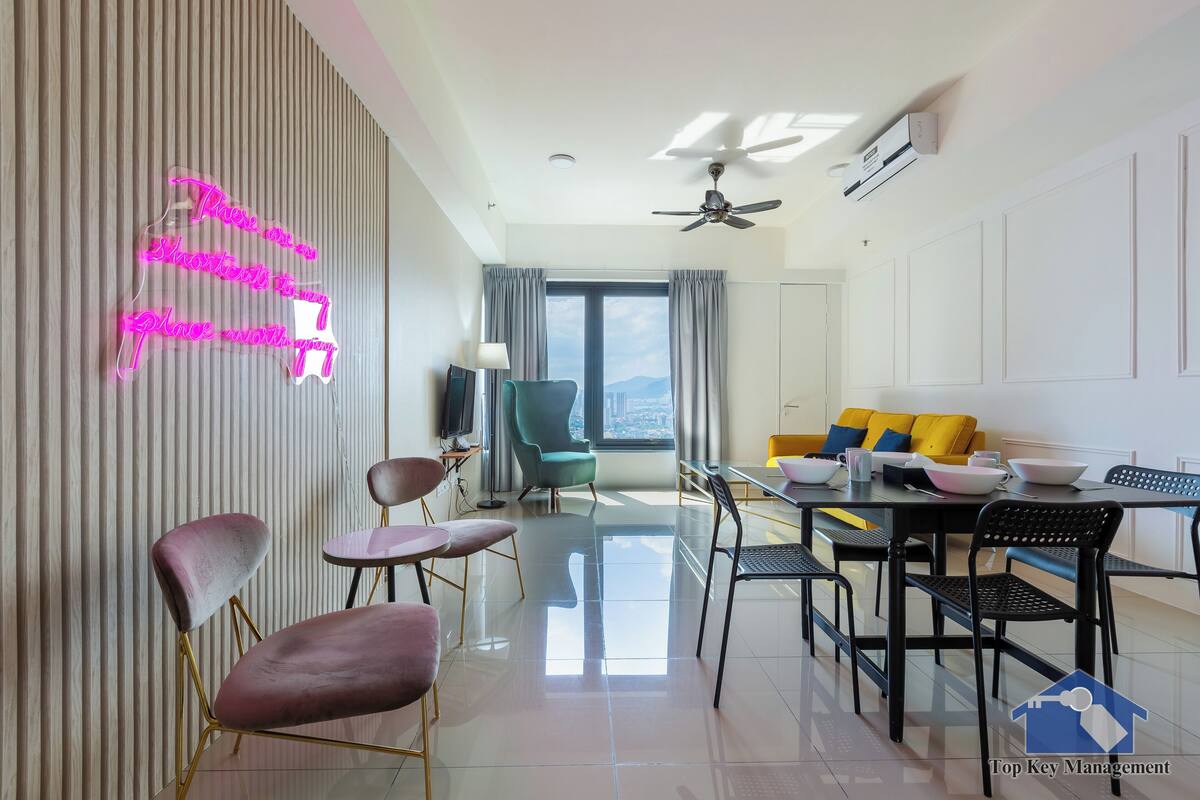 A modern hotel room with a dining area, a large window with curtains, a ceiling fan, and a neon sign on the wall.