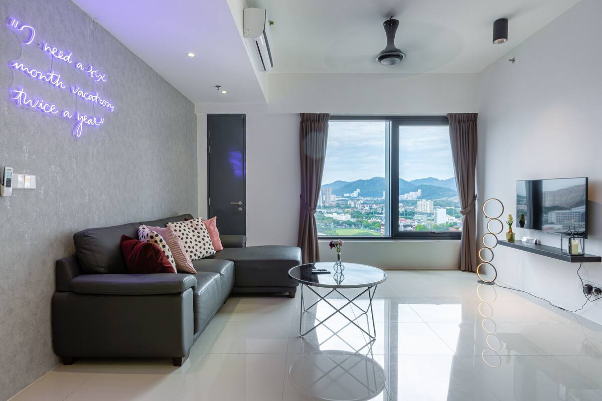 A modern living room with a large window, a sofa, a coffee table, and a neon sign on the wall.