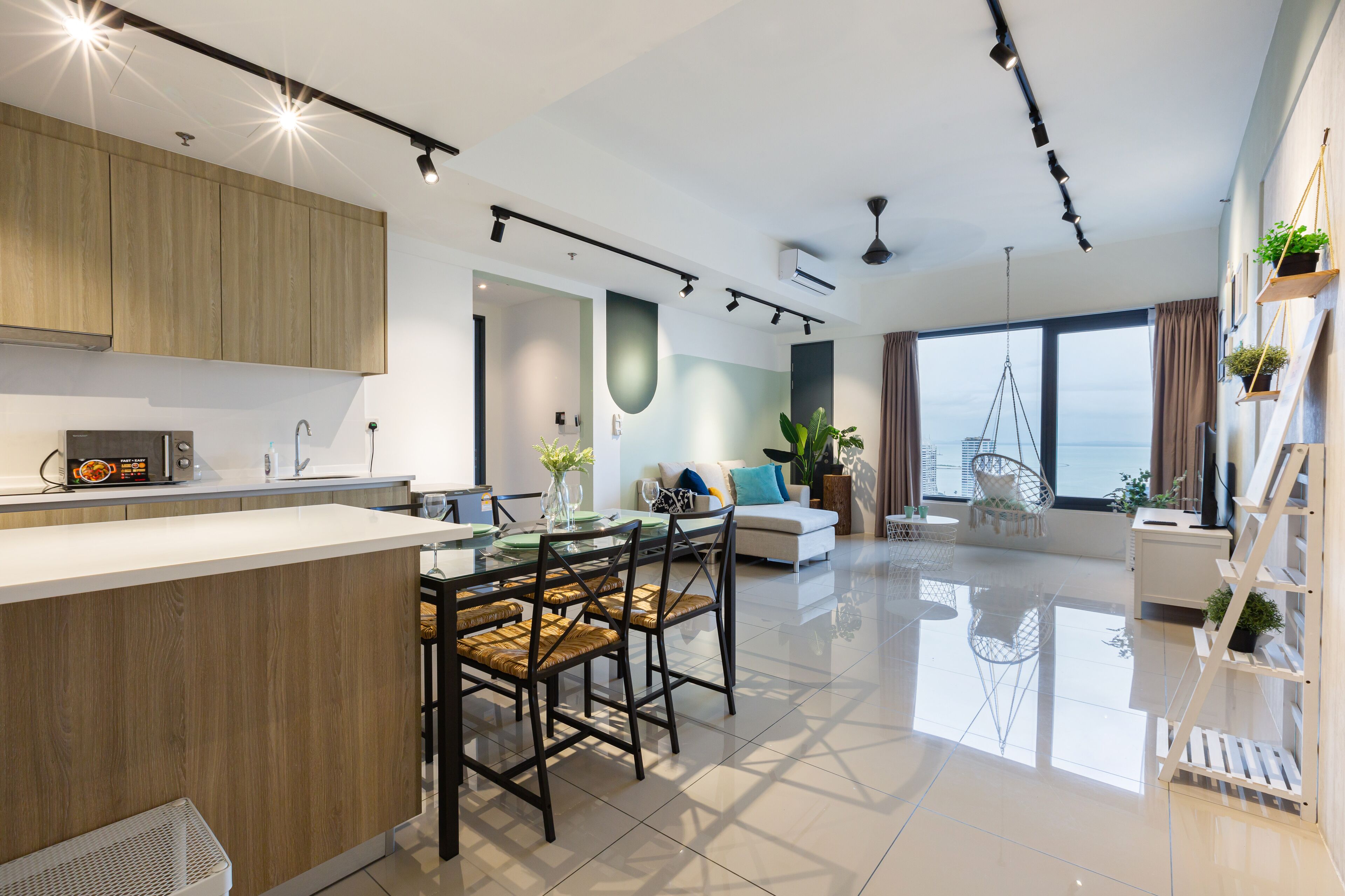 Cocina moderna con una isla central, comedor con sillas y sala de estar con sofá y vistas a la ciudad.