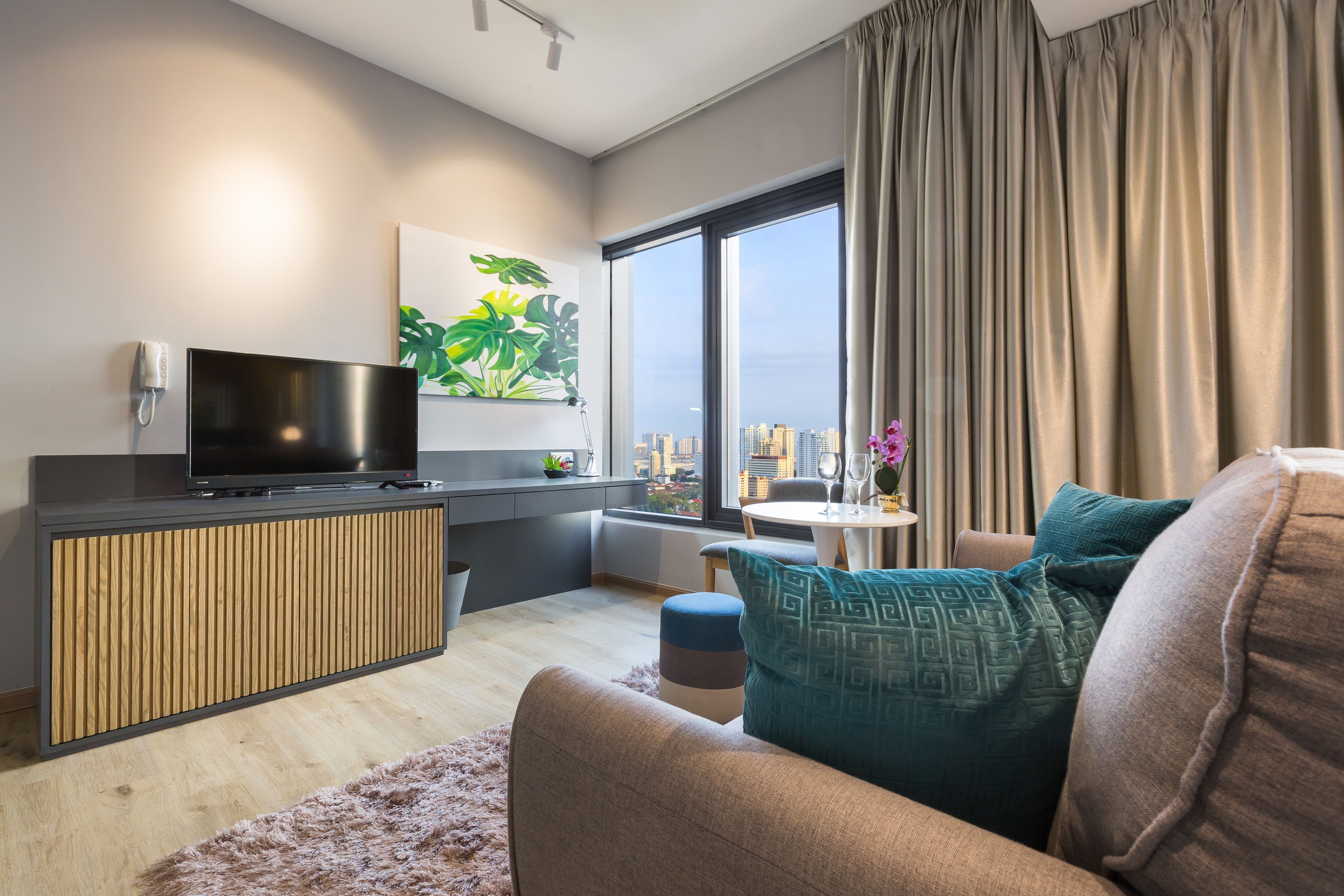 A modern living room with a flat-screen TV, a plant, a city view, and a large window with curtains.