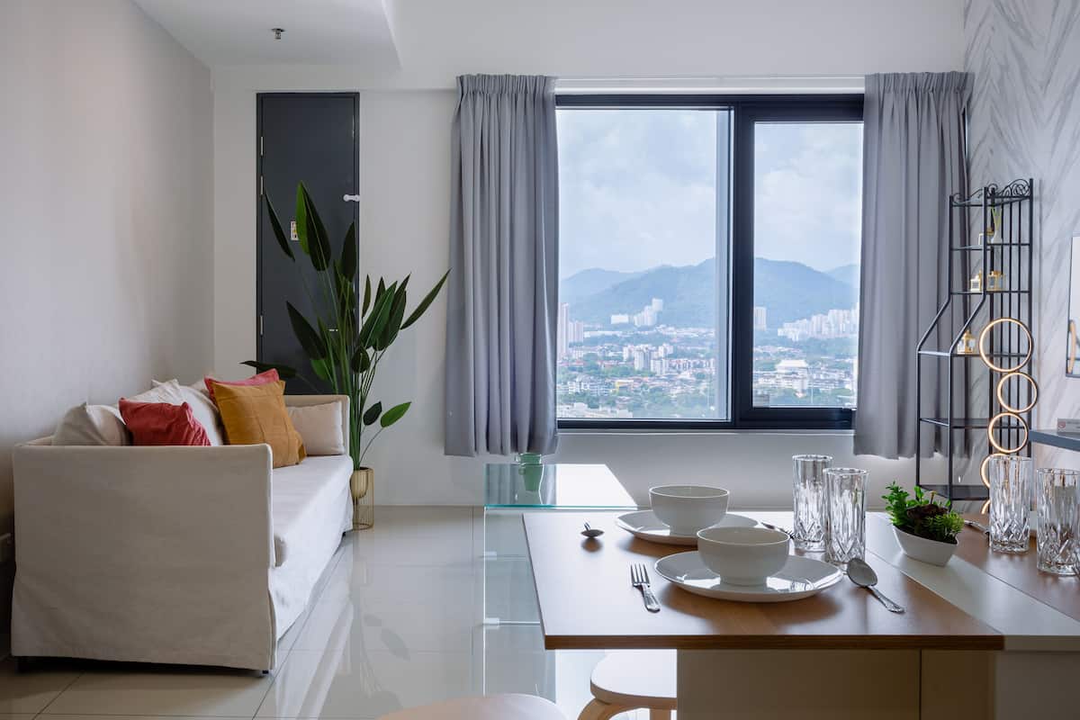 A modern living room with a sofa, dining table, and a view of a cityscape through a large window.