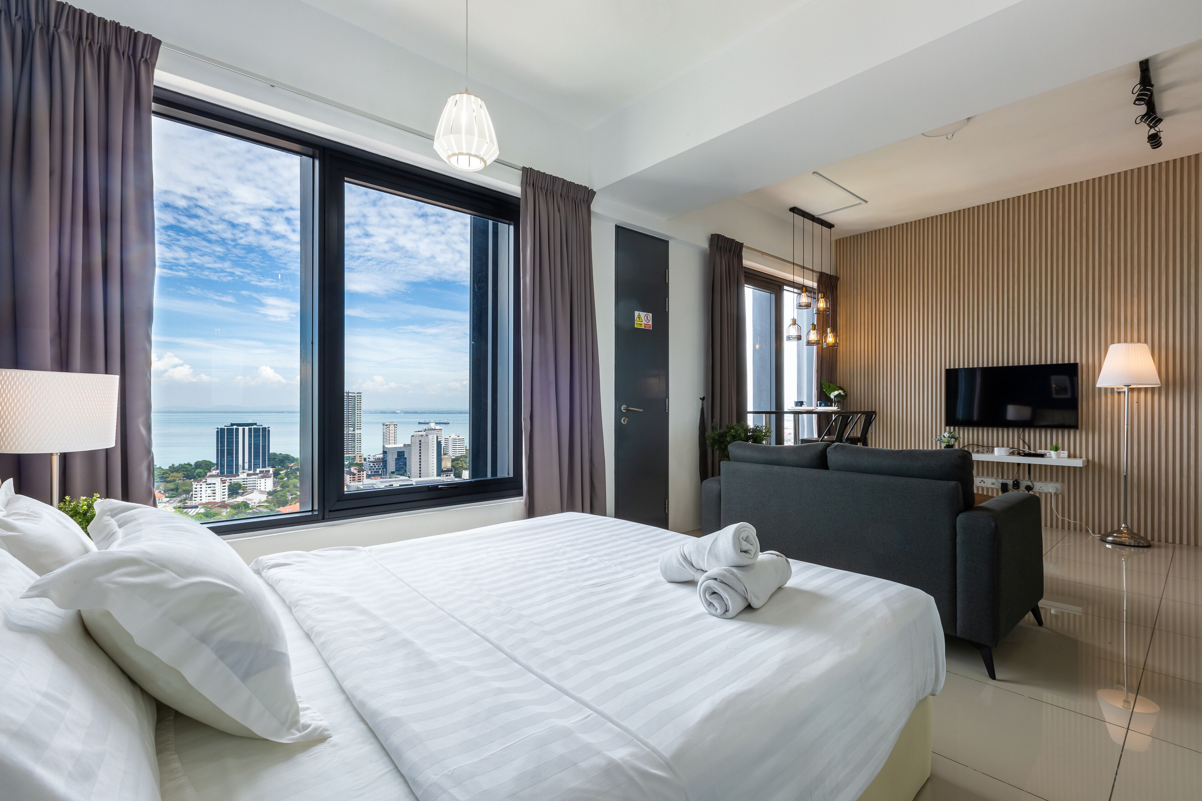 Una habitación de hotel con una cama grande, un sofá, un televisor y vistas a la ciudad.