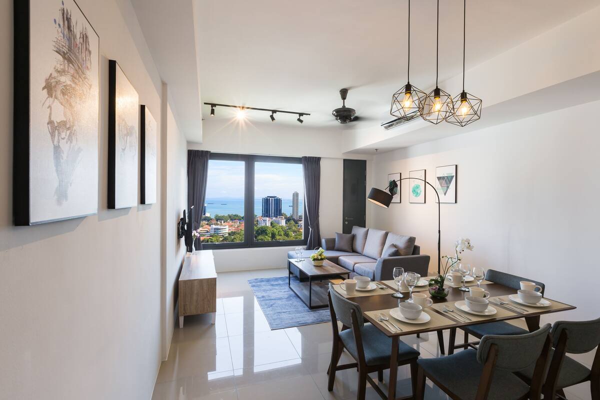 A modern living room with a sofa, dining table set for four, and a large window with a city view.