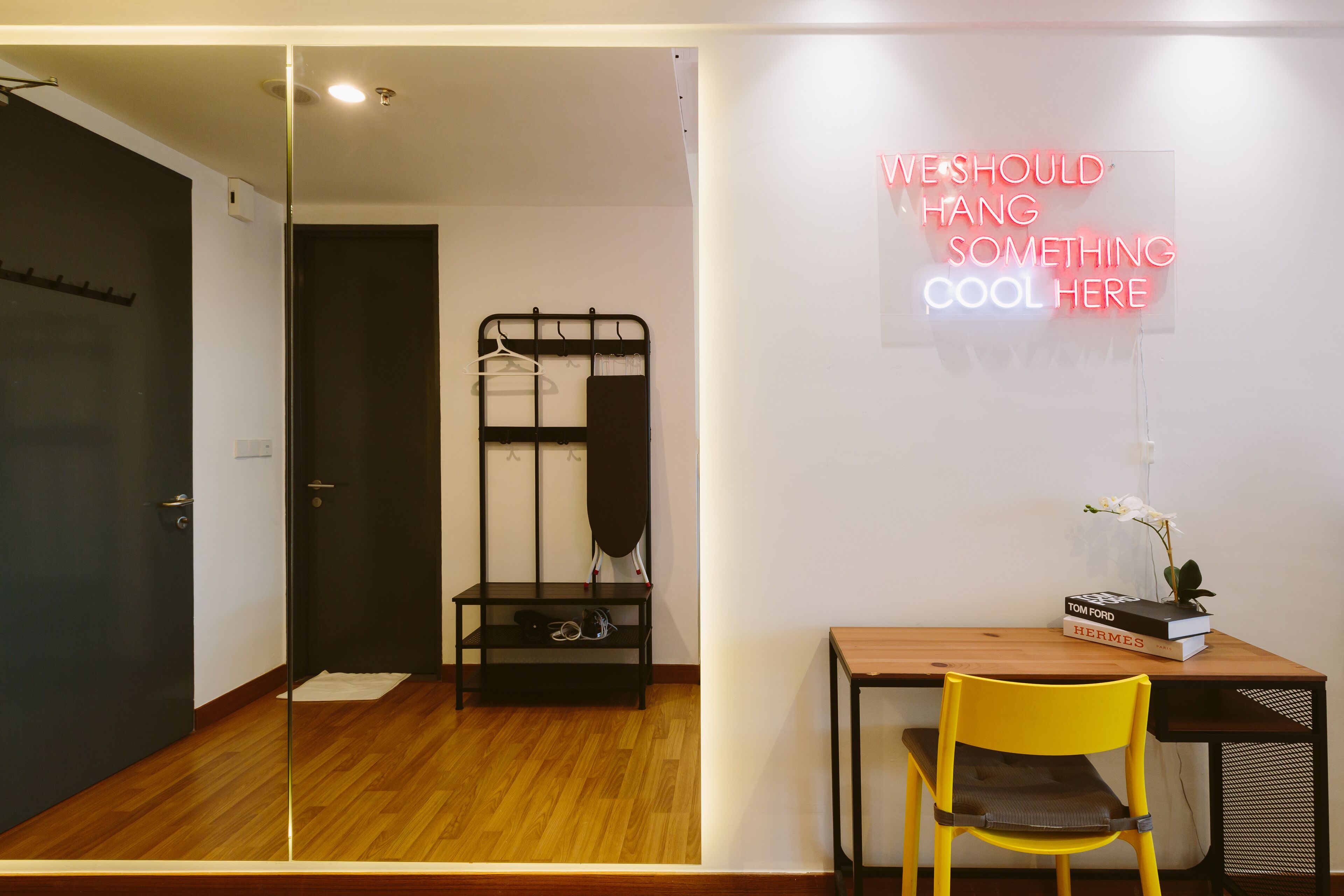 A modern room with a wooden desk, a yellow chair, a black hanger rack, and a neon sign on the wall.