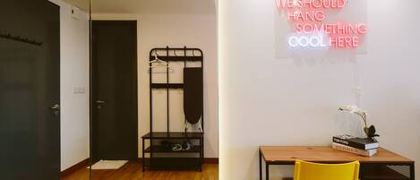 A modern room with a wooden desk, a yellow chair, a black hanger rack, and a neon sign on the wall.