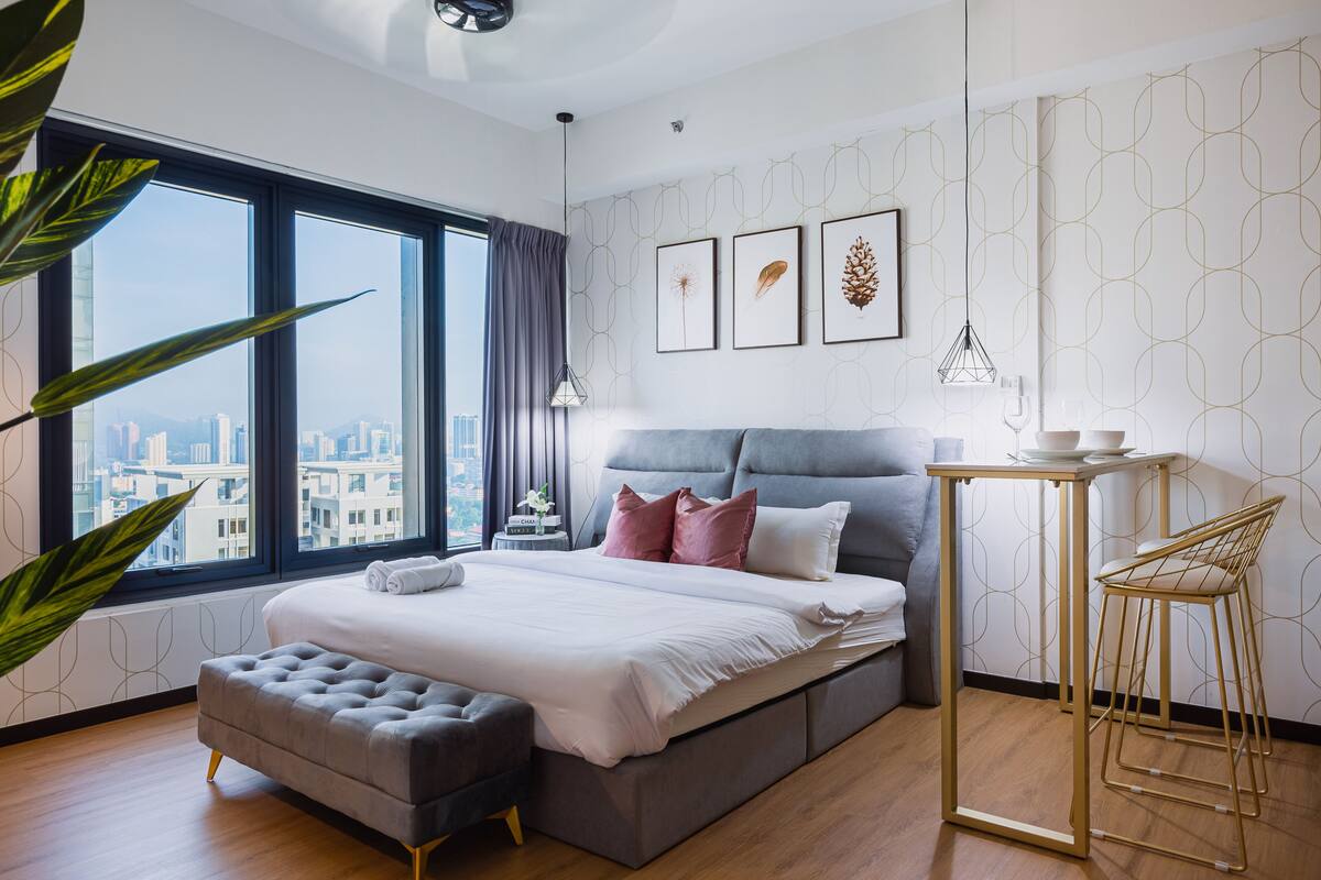 A modern bedroom with a large bed, a side table, a chair, and a view of the city through large windows.