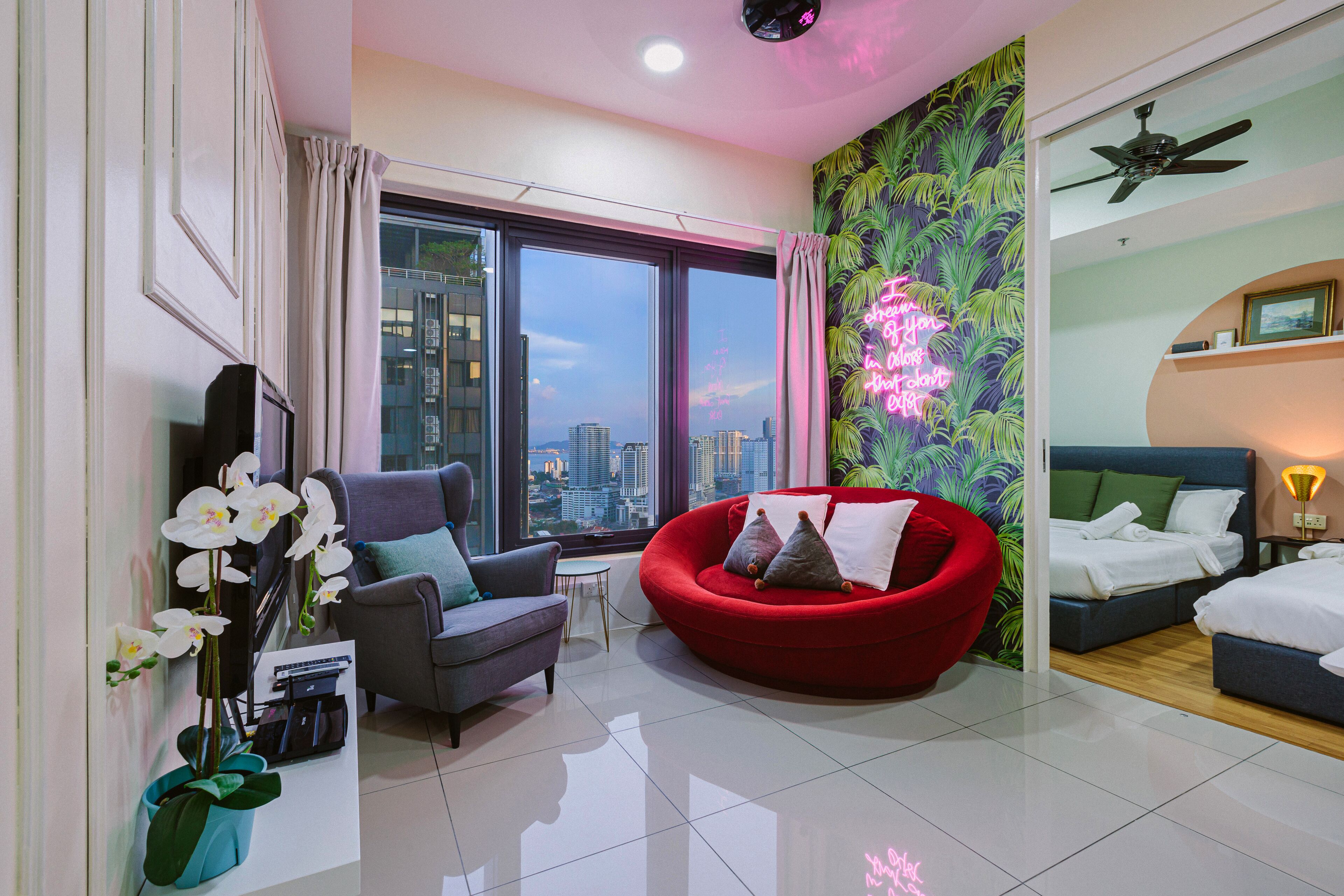 Un hotel moderno con vistas a la ciudad, un sofá rojo, un sillón gris y una cama con sábanas blancas.