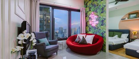 Un hotel moderno con vistas a la ciudad, un sofá rojo, un sillón gris y una cama con sábanas blancas.
