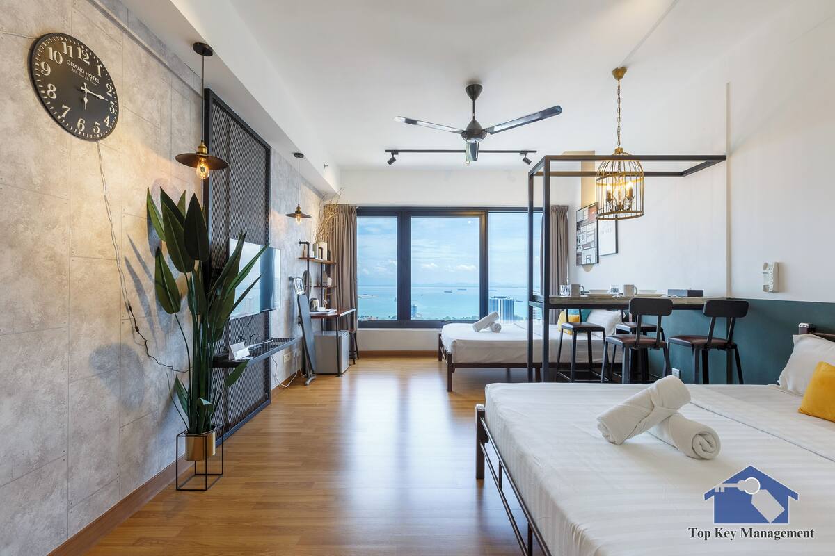 A modern hotel room with a large bed, a desk, and a view of the sea.