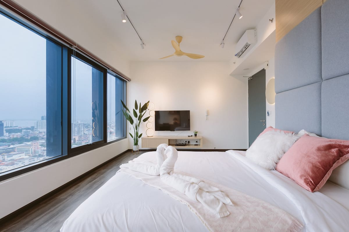 A modern hotel room with a large bed, a flat-screen TV, a ceiling fan, and a city view.
