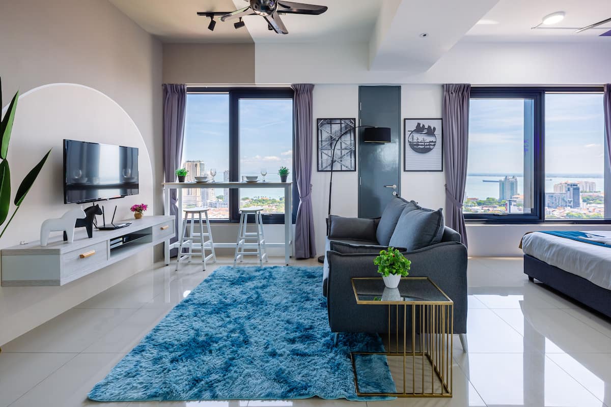 A modern living room with a flat-screen TV, a sofa, a desk, and a large window with a city view.