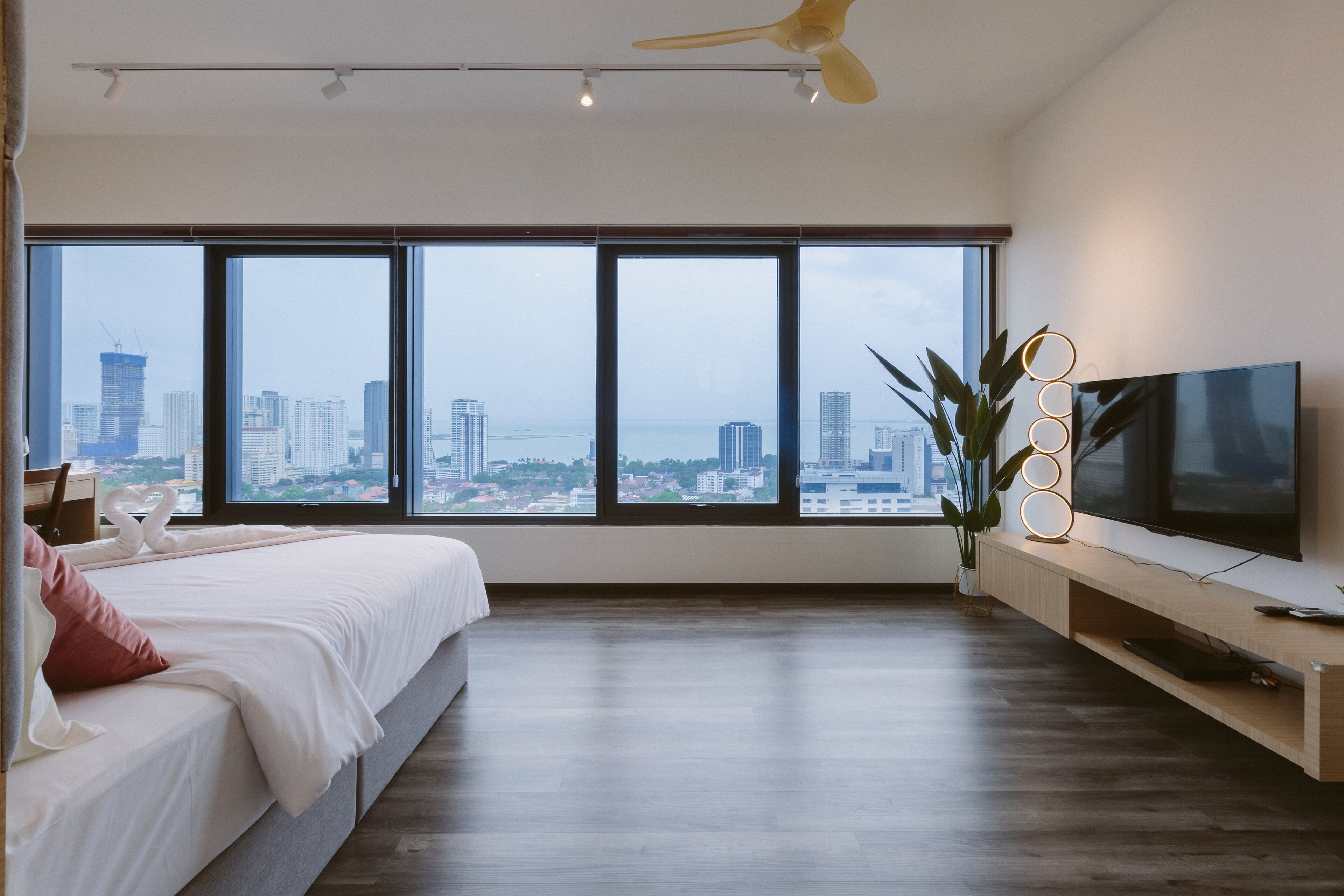 A modern hotel room with a large bed, a flat-screen TV, and a city view through large windows.