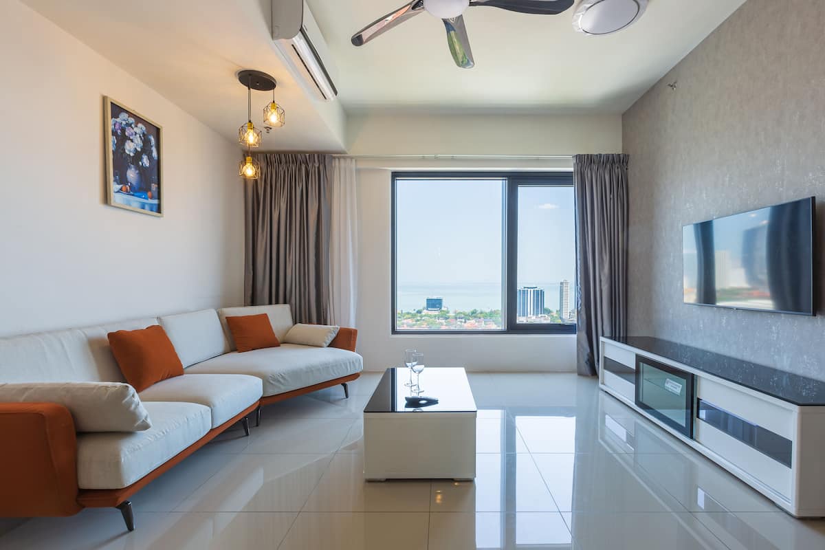 A modern living room with a sofa, a coffee table, a flat-screen TV, and a large window with a view of the city.