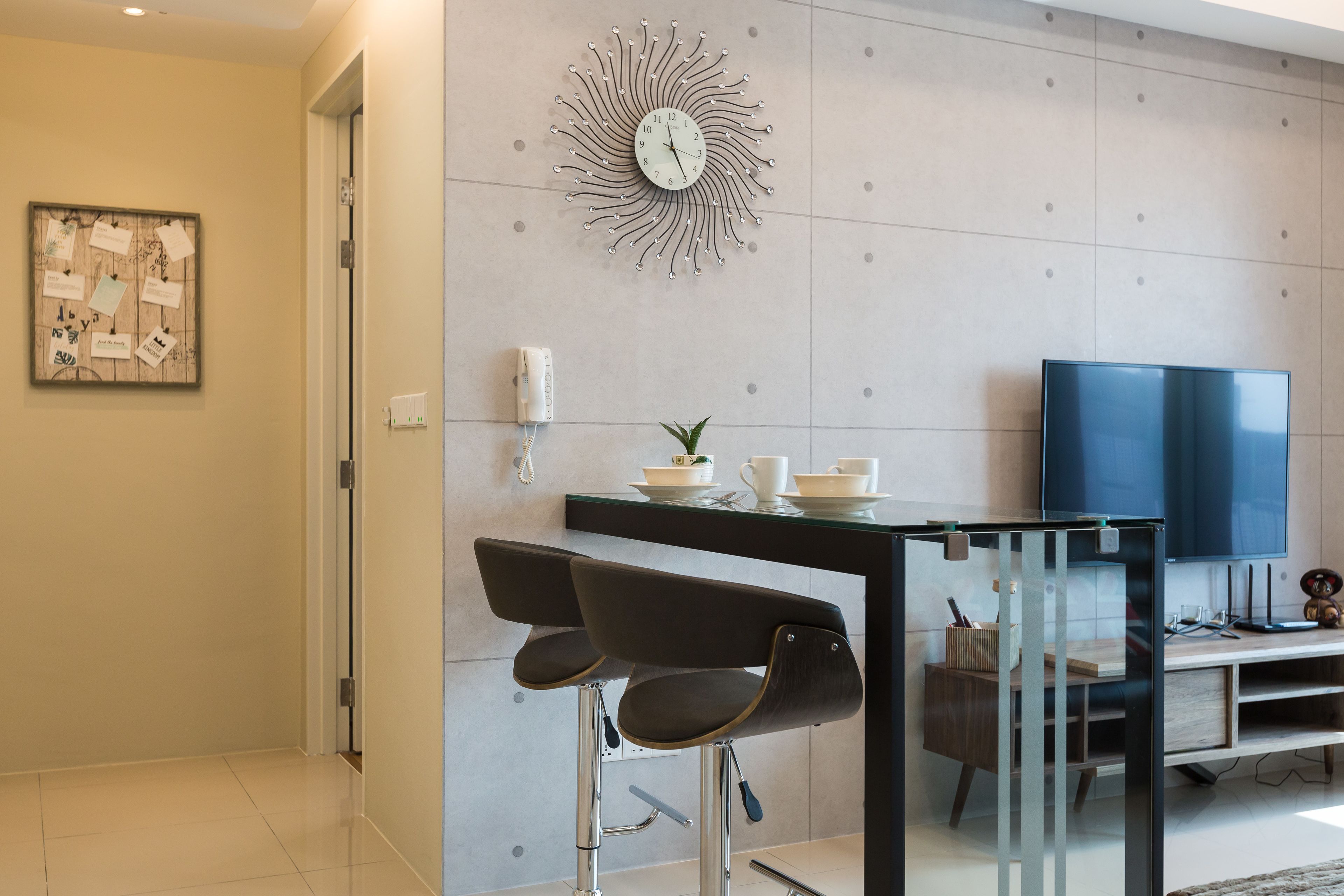 A modern living room with a large flat-screen TV, a decorative wall clock, and a glass coffee table.