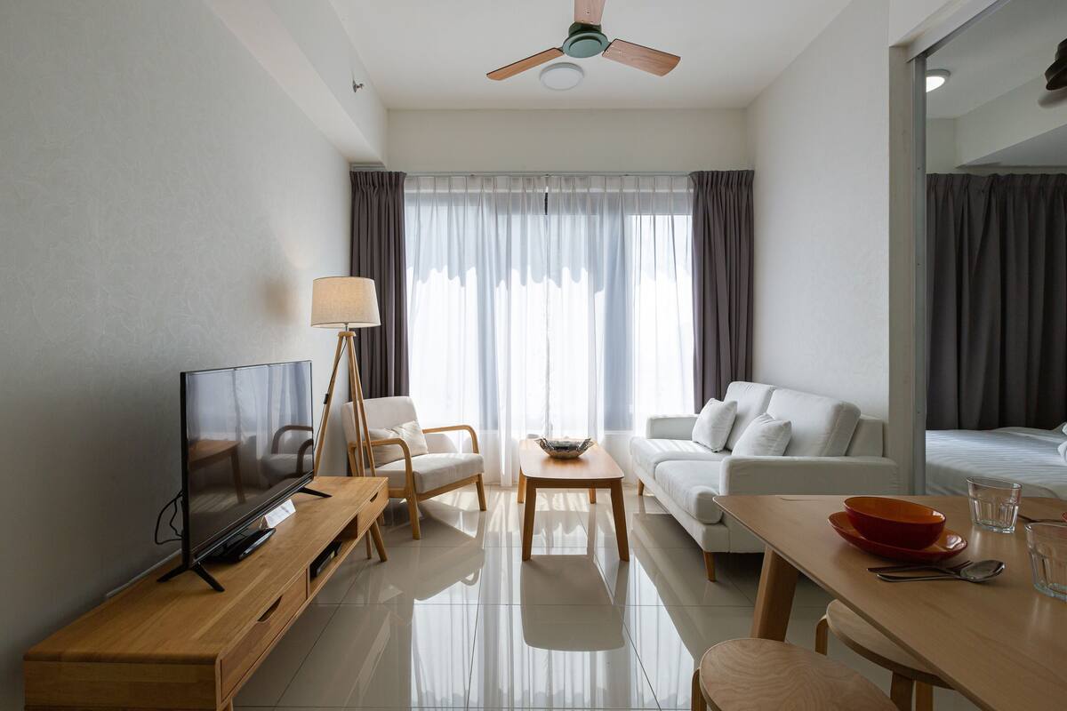 A modern hotel room with a flat-screen TV, a wooden coffee table, a sofa, a dining table, and a ceiling fan.