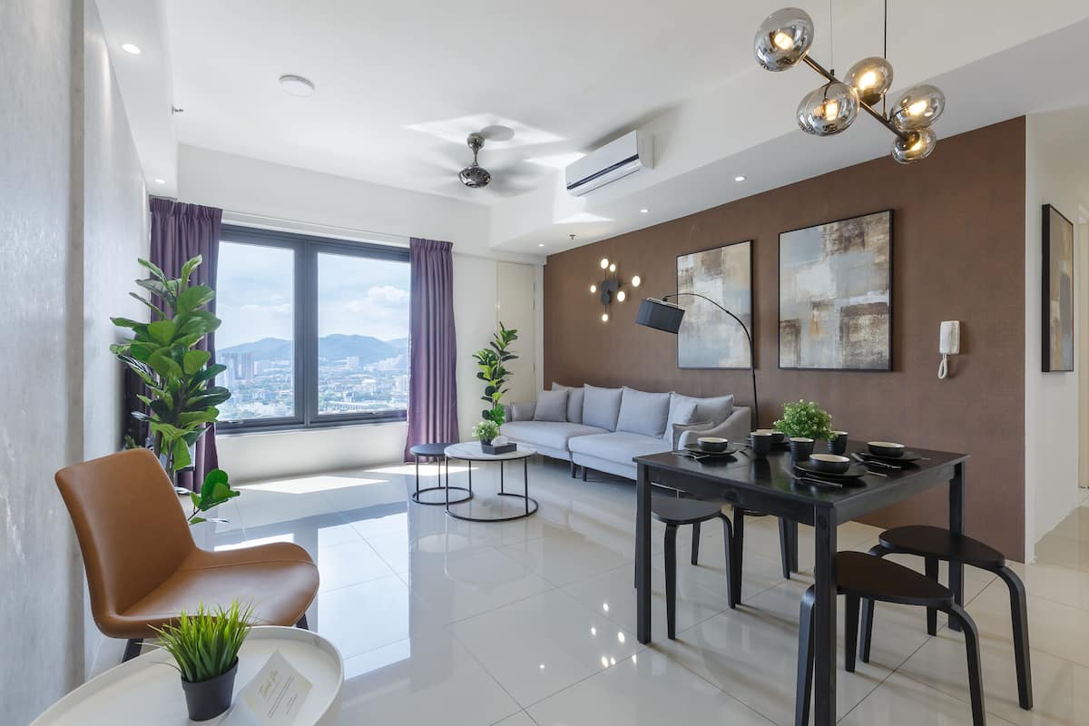 A modern living room with a sofa, dining table, and chairs, a large window with a view, and decorative wall art.