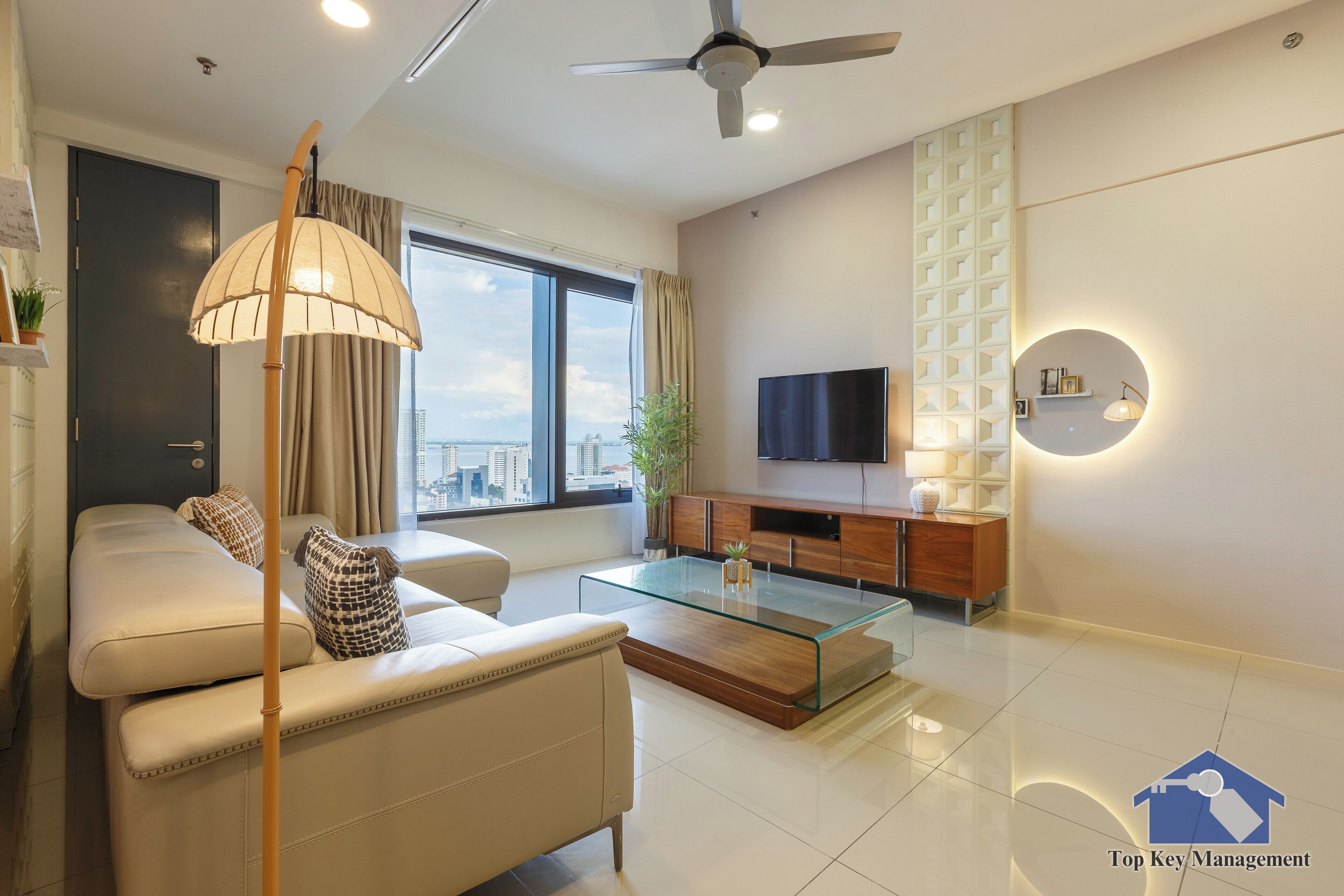 A modern living room with a sofa, a glass coffee table, a TV, and a ceiling fan.