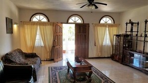 A spacious living room with a large window, a ceiling fan, and a wooden cabinet. - Marantha Close (Montego Bay)
