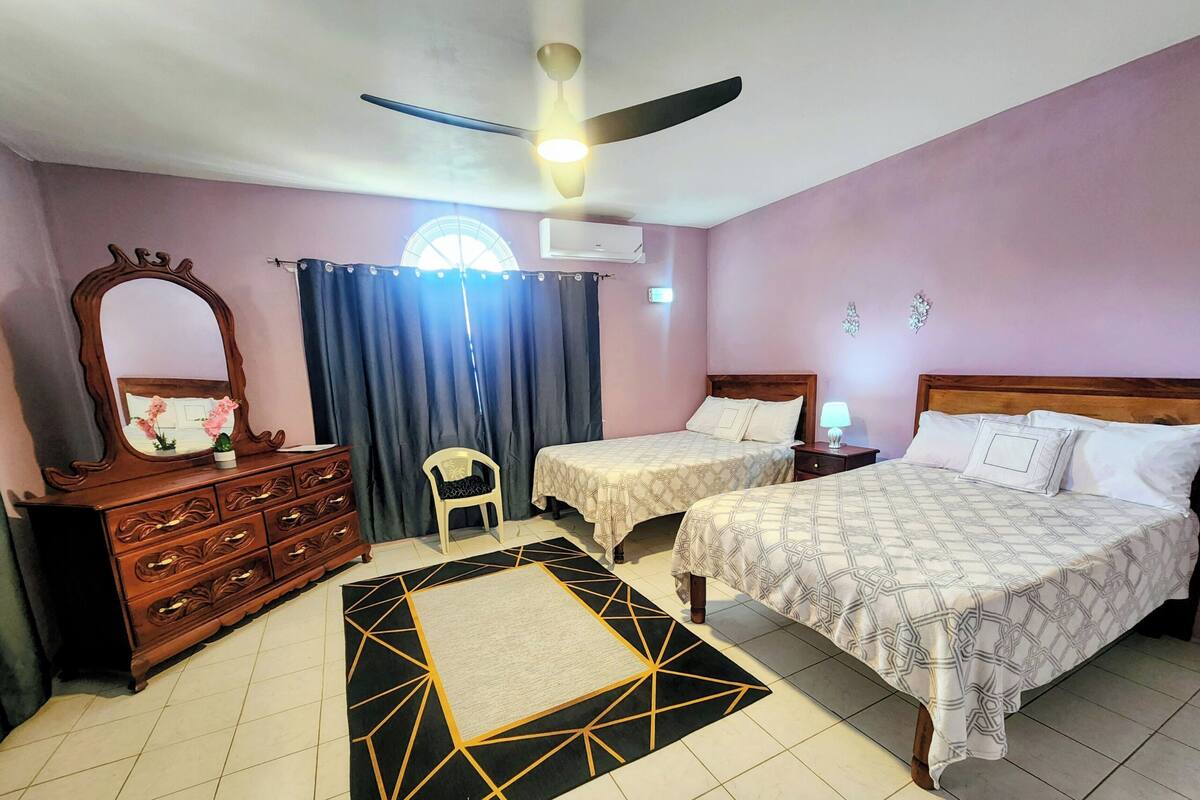 Un dormitorio con dos camas, un aparador, un ventilador de techo y una ventana con cortinas.