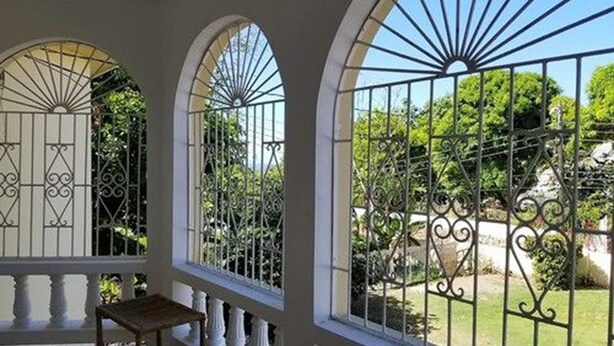 A covered patio with arched windows and a view of a garden. - Marantha Close (Montego Bay)