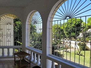 A covered patio with arched windows and a view of a garden. - Marantha Close (Montego Bay)
