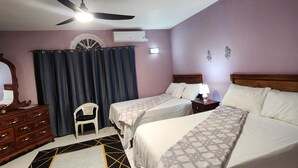A hotel room with two beds, a ceiling fan, an air conditioning unit, a wooden dresser, a chair, and a patterned rug. - Marantha Close (Montego Bay)