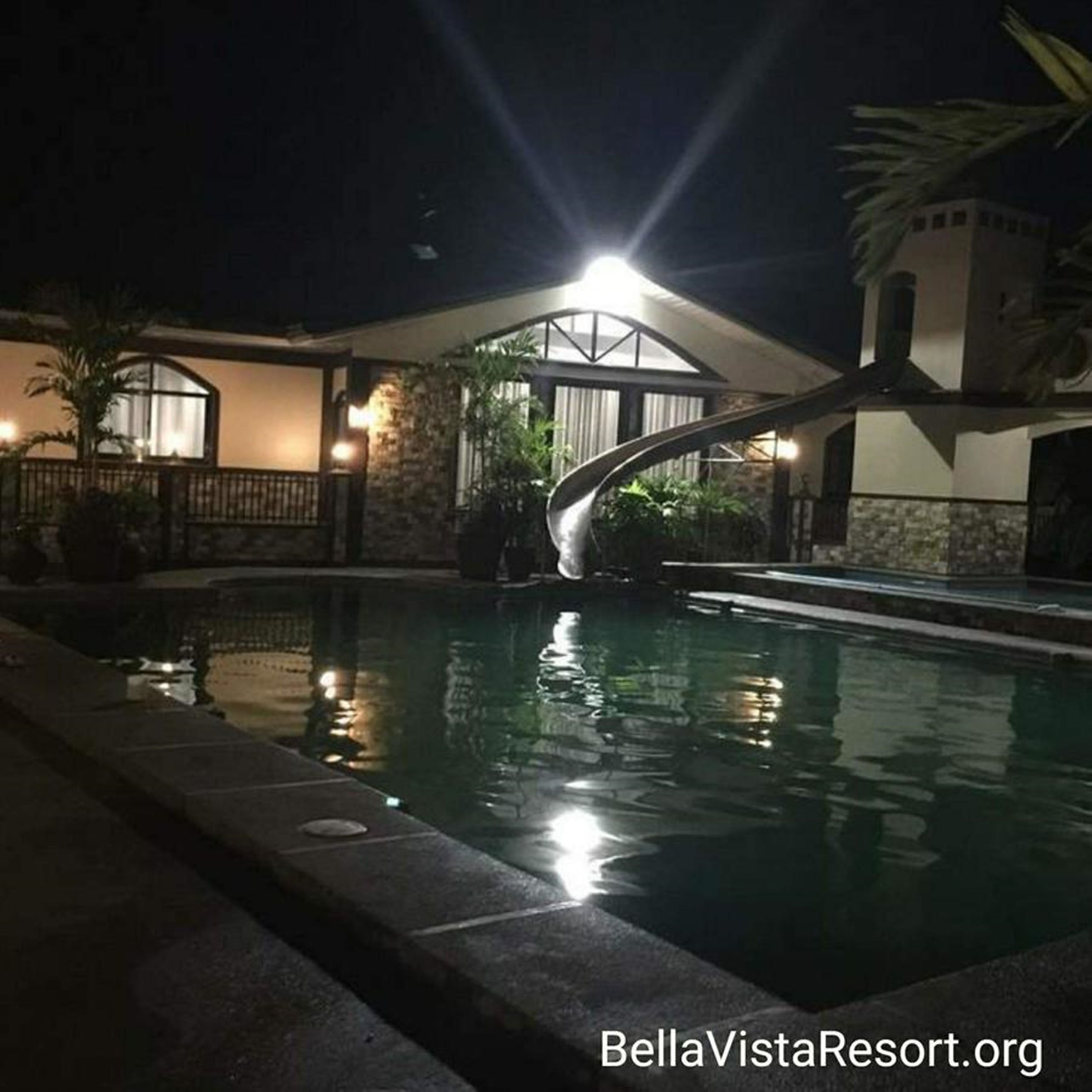 Una piscina con un puente, rodeada de edificios con iluminación cálida.