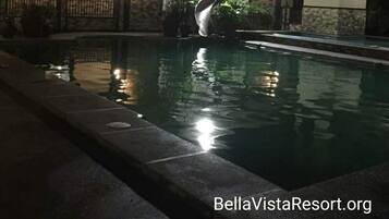 Una piscina con un puente, rodeada de edificios con iluminación cálida.