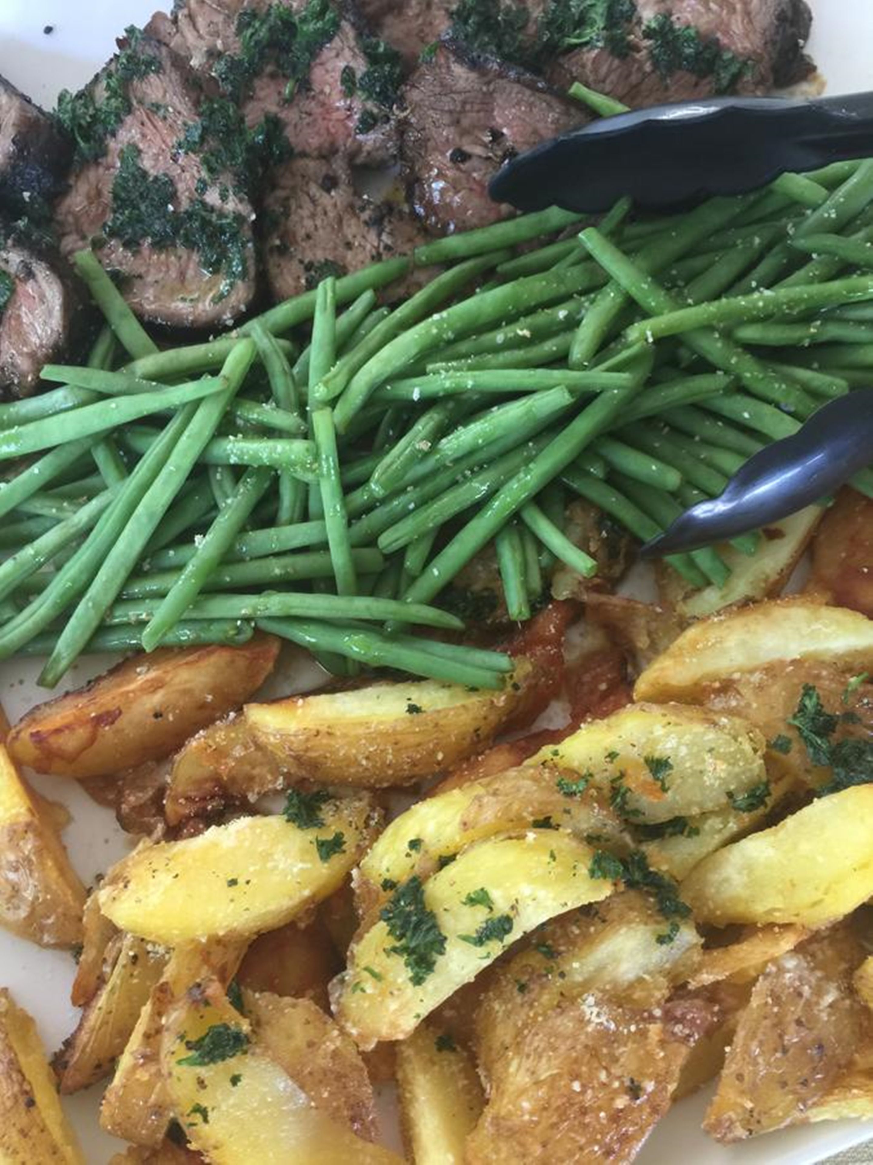 Un plato con bistec en rodajas, judías verdes y patatas asadas.