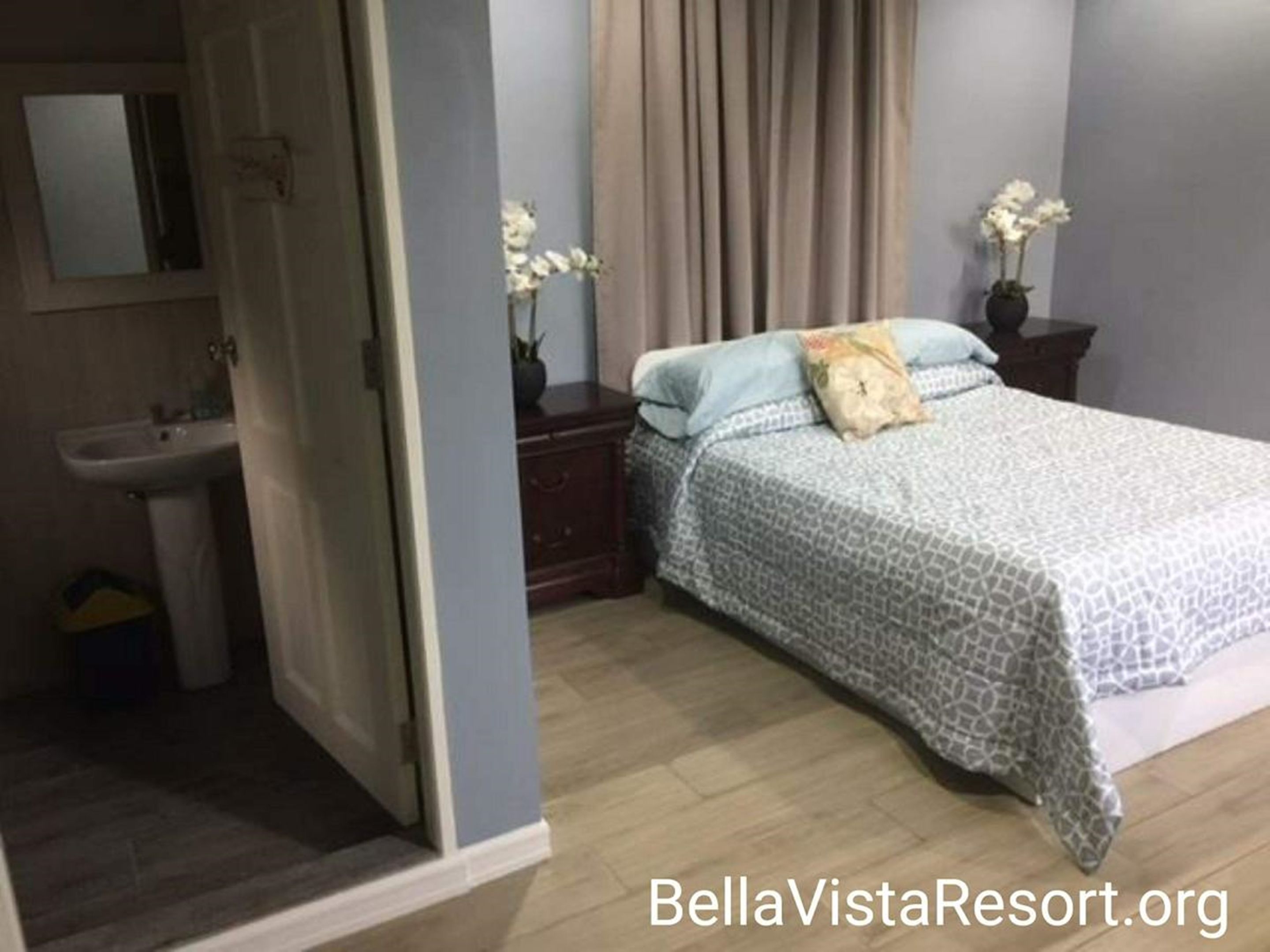 A bedroom with a bed, a nightstand, a dresser, a mirror, and a bathroom with a sink and toilet.