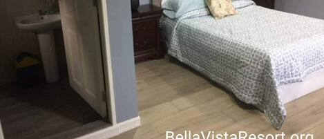 A bedroom with a bed, a nightstand, a dresser, a mirror, and a bathroom with a sink and toilet.