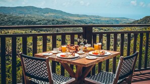 A wooden table set for breakfast with a scenic view of hills and a clear sky. - Chalets Chamarel (Chamarel)