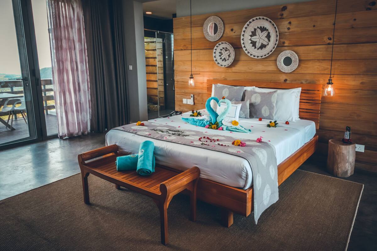 A hotel room with a large bed, wooden headboard, and a wooden bench with towels.
