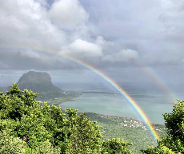 A landscape with a mountain, a rainbow, and a body of water. - Chalets Chamarel (Chamarel)