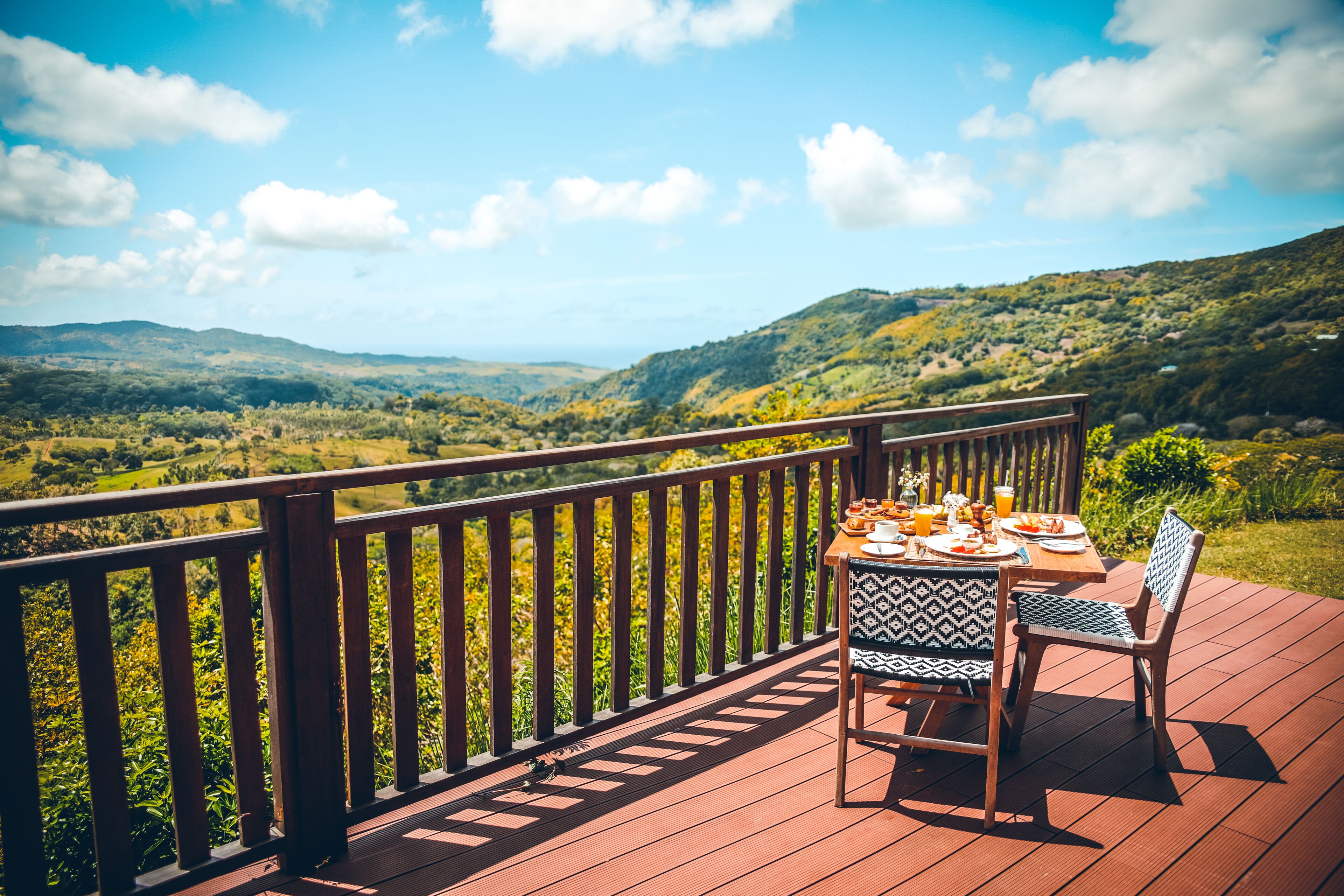 A wooden deck with a table set for a meal, overlooking a lush valley.