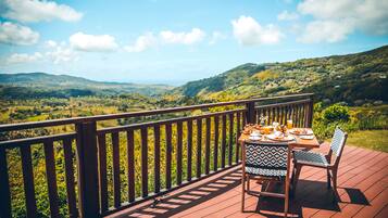 A wooden deck with a table set for a meal, overlooking a lush valley.
