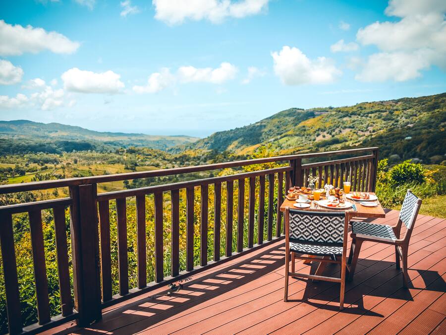 A wooden deck with a table set for a meal, overlooking a lush valley.
