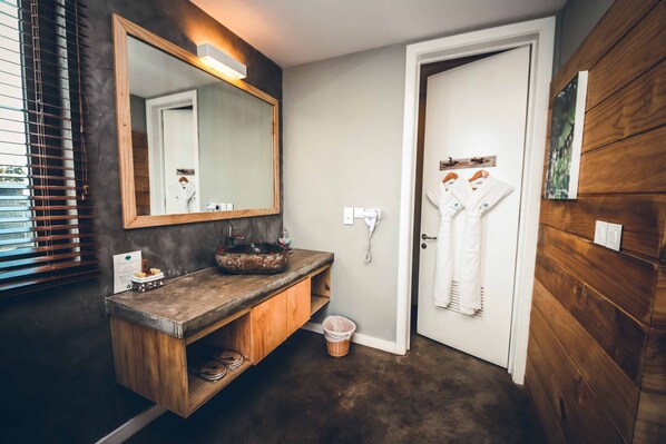 Un baño con tocador de madera, un espejo grande, un lavamanos y una puerta que da a la zona de ducha.
