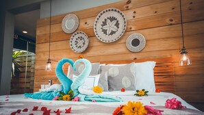 A neatly made bed with a heart-shaped towel arrangement, wooden headboard, and decorative plates. - Chalets Chamarel (Chamarel)