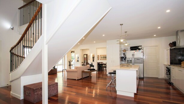 Amplia sala de estar con piso de madera, una escalera, cocina y comedor.