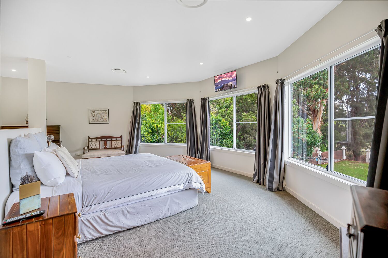 A bedroom with a large bed, a wooden nightstand, a TV, and a window with curtains.